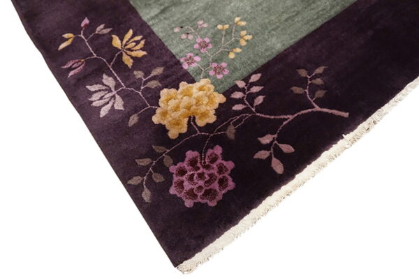 Floral rug detail showing a dark plum border with large flowers bordering a lighter green field.