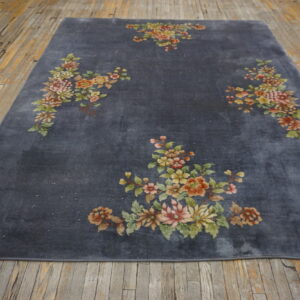 A low-pile charcoal gray area rug featuring large pink and green floral designs on exposed wood flooring.