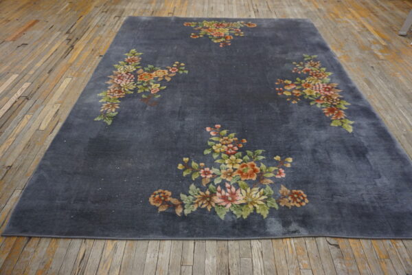 A low-pile charcoal gray area rug featuring large pink and green floral designs on exposed wood flooring.