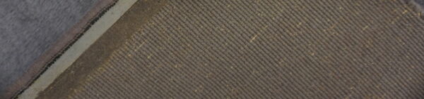 Taupe ribbed rug texture with visible fiber flecks, framed by a contrasting light woven binding.