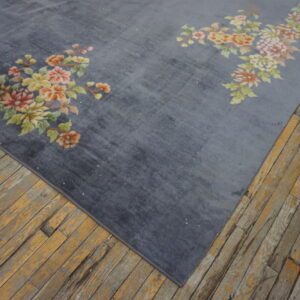 A plush gray rug with traditional pink and yellow floral accents rests on rustic wood flooring.