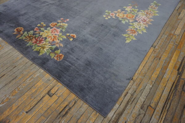 A plush gray rug with traditional pink and yellow floral accents rests on rustic wood flooring.