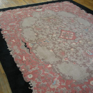 Ornate gray and dusty rose low-pile rug with a wide black border rests on light brown hardwood flooring.