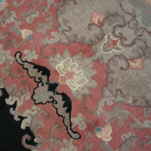 A close-up of a high-pile rug displays a large floral design in dusty rose, taupe, and deep black.