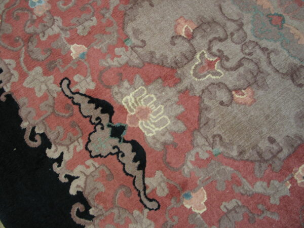 A close-up of a high-pile rug displays a large floral design in dusty rose, taupe, and deep black.