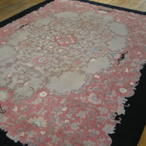 A pink and grey floral area rug with a black border contrasting with the light hardwood flooring.
