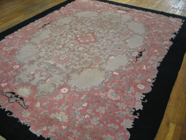 A pink and grey floral area rug with a black border contrasting with the light hardwood flooring.