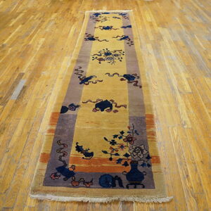 A gold runner rug with dark blue, rust, and brown traditional motifs lies on distressed wooden floors.