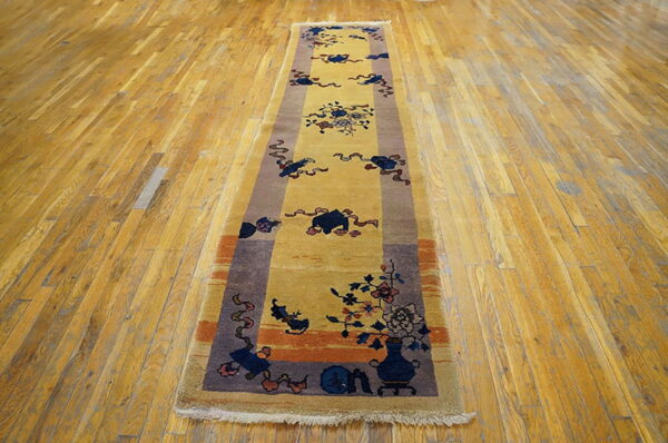 A gold runner rug with dark blue, rust, and brown traditional motifs lies on distressed wooden floors.