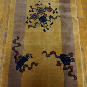 Gold runner rug with brown borders and complex blue and gray symbolic patterns on wood planks.