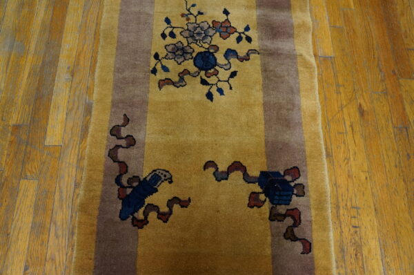 Gold runner rug with brown borders and complex blue and gray symbolic patterns on wood planks.