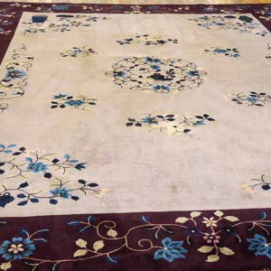 Floral rug with a light field and dark burgundy border featuring blue blossoms on a wood floor.