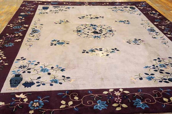 Floral rug with a light field and dark burgundy border featuring blue blossoms on a wood floor.