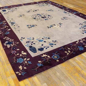 Light gray rug featuring blue floral sprays and a wide, deep purple patterned border on wood floors.