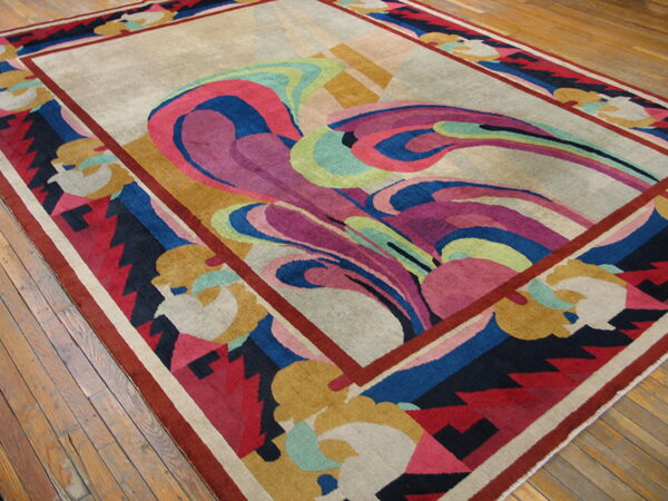 Low-pile rug with flowing magenta, blue, and green abstract patterns on a beige field, resting on wood floors.