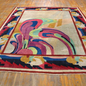 Abstract area rug featuring swirling pink and blue central motifs and a multi-colored geometric border on wood.