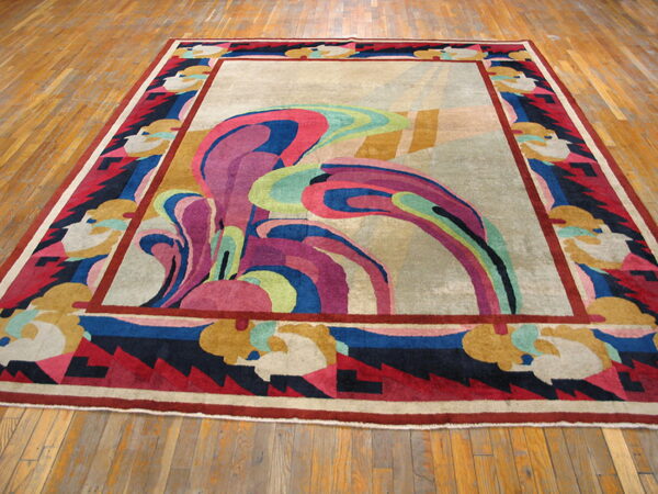 Abstract area rug featuring swirling pink and blue central motifs and a multi-colored geometric border on wood.