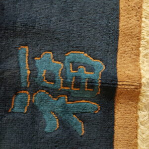 Dark blue rug detail shows teal and orange abstract symbols, red accents, and a tan fringed border.