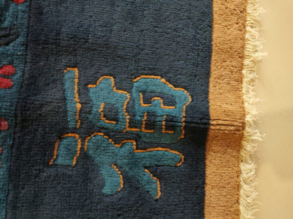 Dark blue rug detail shows teal and orange abstract symbols, red accents, and a tan fringed border.
