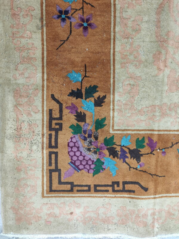 Rust field rug corner with purple and teal florals, geometric black trim, and a pale pink scrolled border.