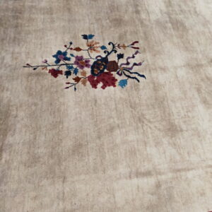Low-pile beige rug featuring a central multicolored floral spray and wide red and dark blue patterned borders.