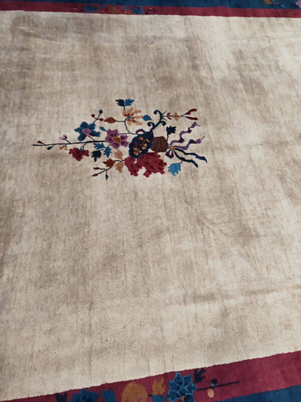 Low-pile beige rug featuring a central multicolored floral spray and wide red and dark blue patterned borders.