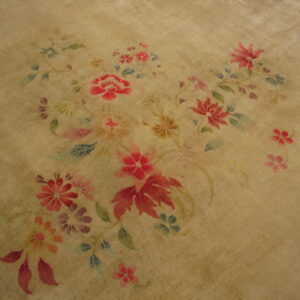 Muted tan rug surface detailed with a central arrangement of red, pink, blue, and green floral motifs.