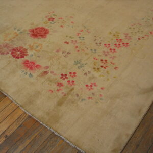 Tan low-pile rug with flowing pink and red floral accents rests on distressed wooden floorboards.