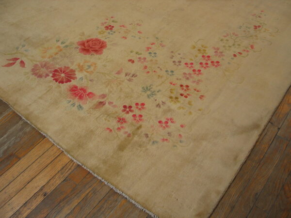 Tan low-pile rug with flowing pink and red floral accents rests on distressed wooden floorboards.
