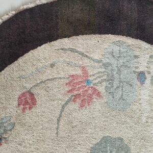 Detailed view of a beige rug section with pink flowers and gray stems next to a dark brown edge.