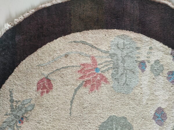Detailed view of a beige rug section with pink flowers and gray stems next to a dark brown edge.