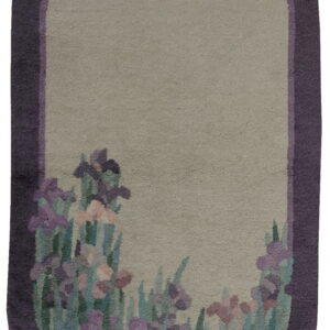 Oblong rug with a deep purple frame, sage green field, and a colorful floral iris pattern.