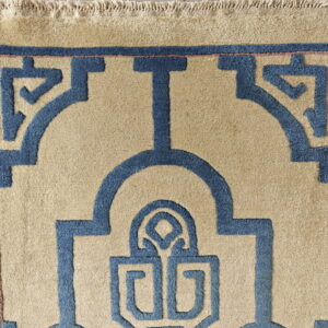 Textured beige rug with bold blue geometric design, thin pink outline, and visible fringes.