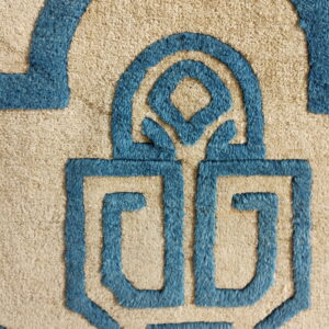 Close-up of a sculpted rug featuring beige texture and raised blue geometric key patterns.