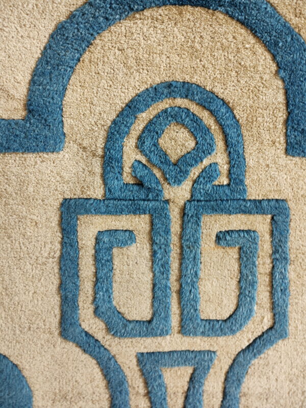 Close-up of a sculpted rug featuring beige texture and raised blue geometric key patterns.