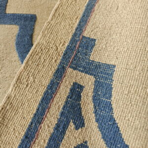 A close-up view of a folded beige and blue rug with large geometric shapes and woven texture.