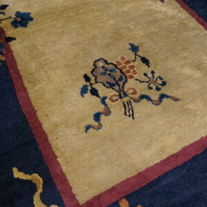 High-pile tan rug with detailed blue and maroon floral borders resting on hardwood flooring.