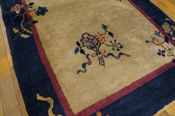 High-pile tan rug with detailed blue and maroon floral borders resting on hardwood flooring.