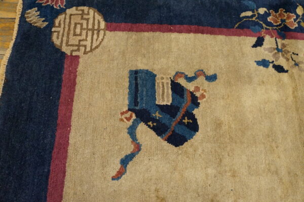 Close-up of a rug with a tan field, navy and pink border, and blue patterned motif.