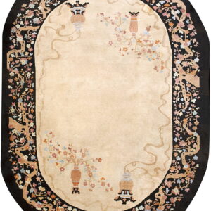 Beige oval rug with black border featuring stylized flowering tree branches and decorative urns.