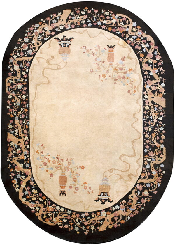 Beige oval rug with black border featuring stylized flowering tree branches and decorative urns.
