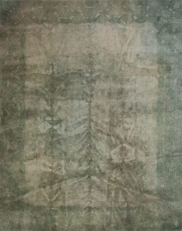 Distressed green rug with a faded floral border surrounding a lighter central field of subtle pattern.