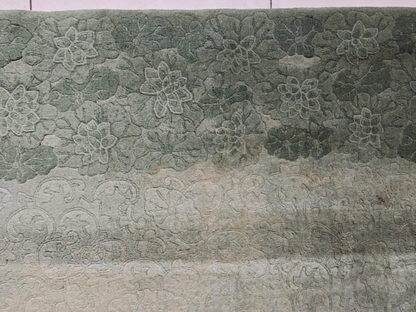 Textured green rug with carved floral pattern and an ombre effect fading into light beige.