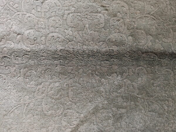 Grey low-pile rug with tone-on-tone carved floral and vine details and a horizontal crease visible.