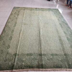Textured green rug with a dark moss floral border and light sage center resting on white tiled flooring.