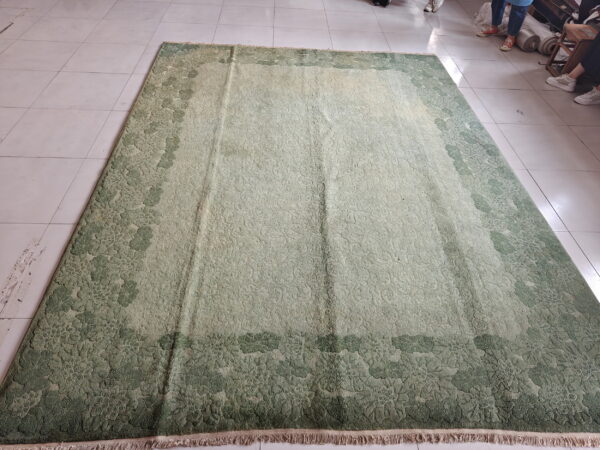 Textured green rug with a dark moss floral border and light sage center resting on white tiled flooring.