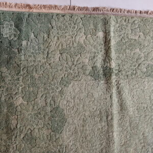 Textured green rug featuring an all-over raised floral design and short fringe on a light tiled floor.