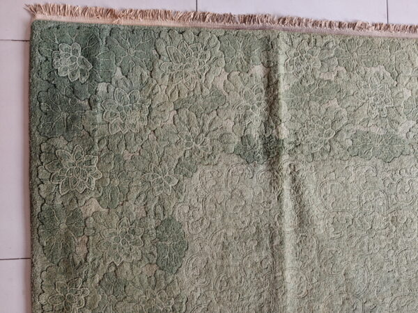 Textured green rug featuring an all-over raised floral design and short fringe on a light tiled floor.