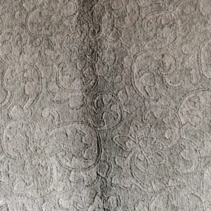 Dense, textured gray rug featuring an embossed traditional scrollwork pattern and a central darker line.