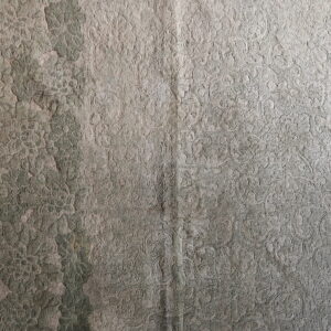 Close-up of a distressed green and gray rug with a high-low floral and scroll pattern texture.